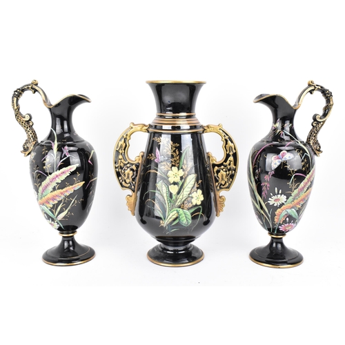 225 - A late Victorian trio of enamelled pottery, comprising a central vase and two jugs, each decorated w... 