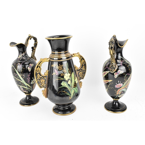 225 - A late Victorian trio of enamelled pottery, comprising a central vase and two jugs, each decorated w... 