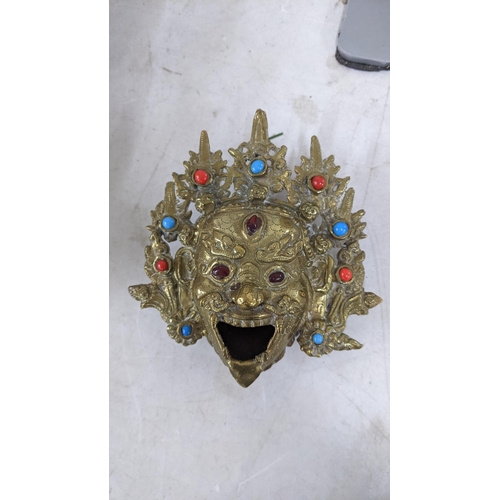 140 - An Oriental gilt metal incense burner cast as the head of Mahakala, together with a Buddha head and ... 