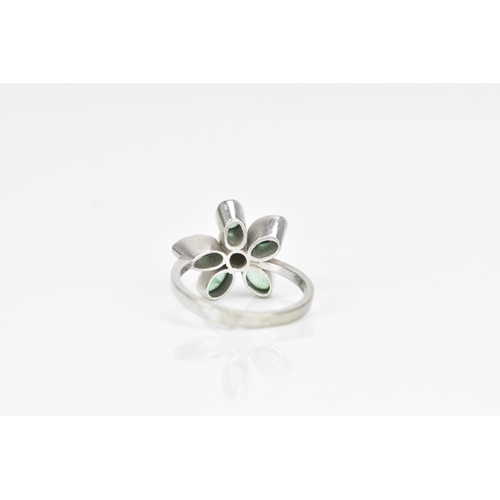 375 - A white metal, emeralds and diamond floral ring, with central bezel set brilliant cut diamond in a s... 