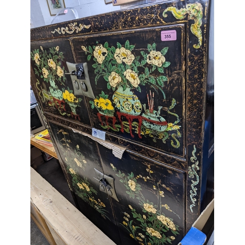 355 - A Chinese black lacquered and painted side cabinet with floral design to the lower doors, the upper ... 