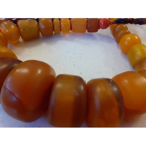 69 - A vintage brown amber necklace together with two native necklaces of reconstructed amber and other b... 