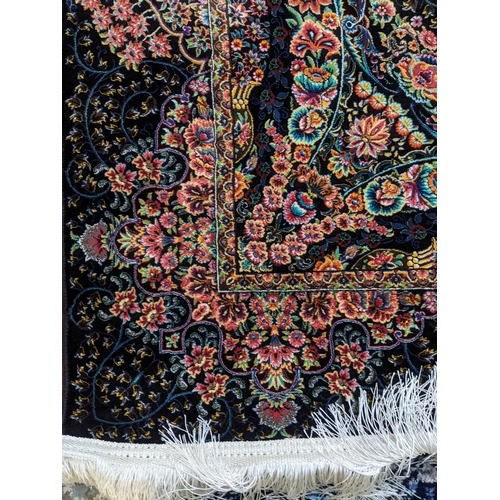 105 - A contemporary small Persian style rug, machine woven on a black ground, floral pattern with a borde... 