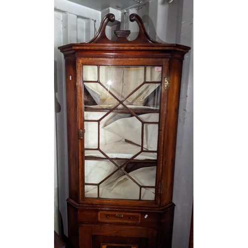 97 - A George III mahogany and boxwood inlaid corner cabinet having a broken swan neck pediment above gla... 