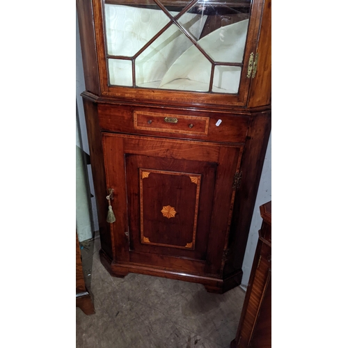 97 - A George III mahogany and boxwood inlaid corner cabinet having a broken swan neck pediment above gla... 