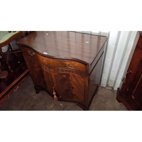 99 - A reproduction mahogany serpentine fronted cabinet having a single drawer above two cupboard doors, ... 