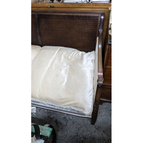 301 - A 1920s cane two-seater sofa with loose cushions, castors missing, ram's head arms and blind fretwor... 