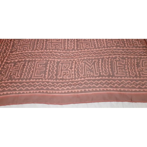 140 - Hermes- A fine silk chiffon wrap in rust and salmon colours, having large capital letters within the... 