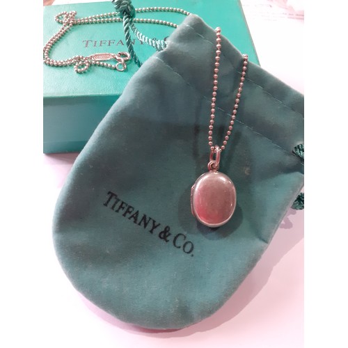 141 - Tiffany-A silver necklace having a ball chain and a small oval shaped locket with makers mark stampe... 