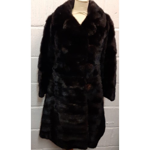 164 - A 1960's black mink knee-length coat having 6 fur covered buttons and a black silk lining with pleat... 