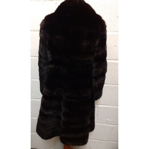 164 - A 1960's black mink knee-length coat having 6 fur covered buttons and a black silk lining with pleat... 