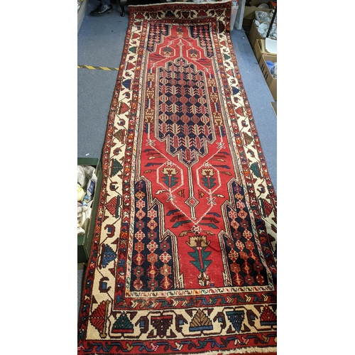 414 - An Iranian hand woven runner having a red ground with a central motif, repeating patterns and tassel... 