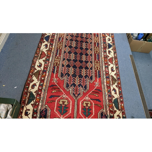 414 - An Iranian hand woven runner having a red ground with a central motif, repeating patterns and tassel... 