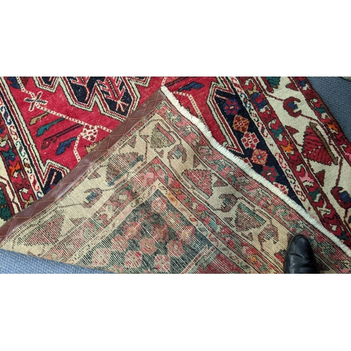 414 - An Iranian hand woven runner having a red ground with a central motif, repeating patterns and tassel... 