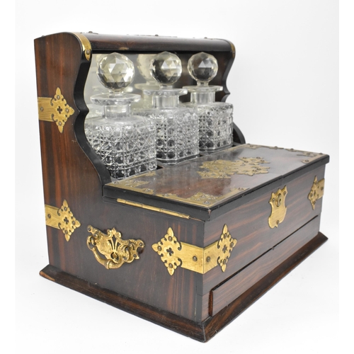 202 - A late Victorian brass-clad coromandel veneered tantalus, comprising three cut glass decanters, mirr... 