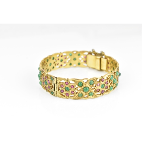 194 - An Indian gold plated, ruby and emerald set bangle, with pierced floral fretwork design inset with r... 