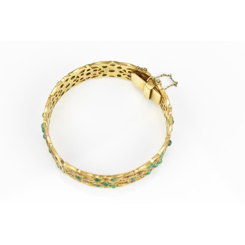 194 - An Indian gold plated, ruby and emerald set bangle, with pierced floral fretwork design inset with r... 