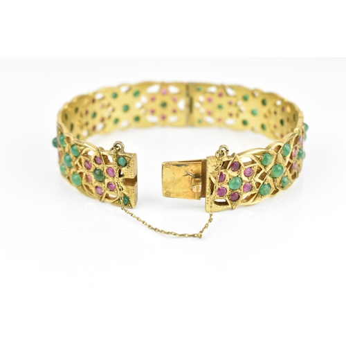 194 - An Indian gold plated, ruby and emerald set bangle, with pierced floral fretwork design inset with r... 