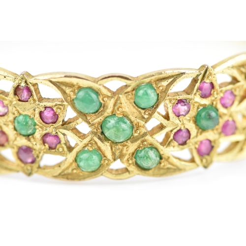 194 - An Indian gold plated, ruby and emerald set bangle, with pierced floral fretwork design inset with r... 