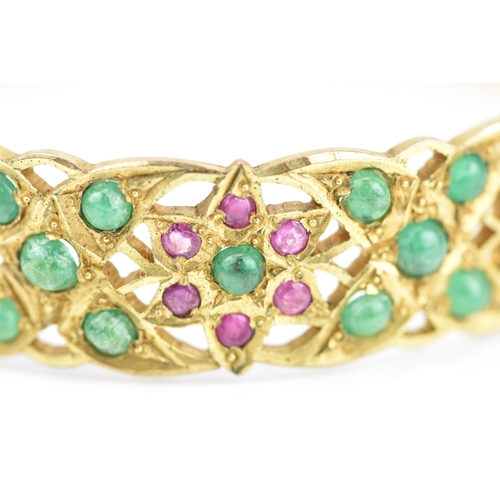 194 - An Indian gold plated, ruby and emerald set bangle, with pierced floral fretwork design inset with r... 