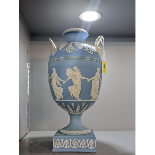 496 - A blue and white Wedgwood jasperware twin handled urn vase decorated with maidens, raised on a squar... 