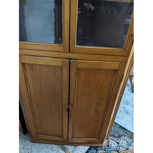 423 - A 19th century pine corner cabinet, twin glazed doors, with shaped internal shelves, over twin field... 