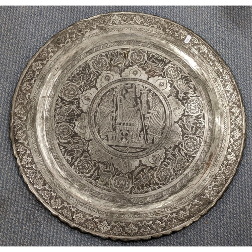 472 - An early 20th century Middle Eastern silver coloured charger decorated with a scene of figures to th... 