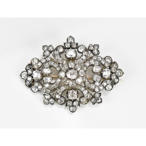 An Edwardian white metal diamond encrusted brooch, set with various sized old mine cut diamonds, the central freeform stone in a floral cluster with c-scrolls and leaves, the back with rose metal catch and hinged pin, 5 cm wide
 Location:CAB 1