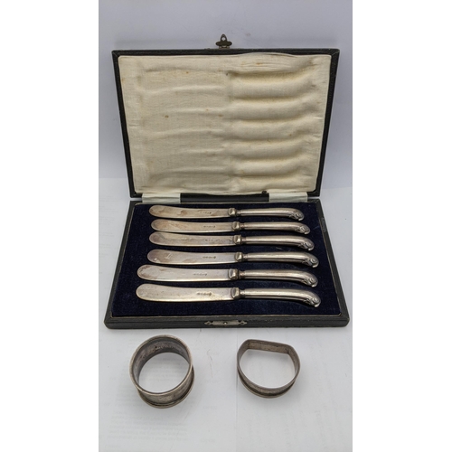 78 - Two silver napkin rings 29.5g together with a cased set of six silver handled butter knives 
Locatio... 