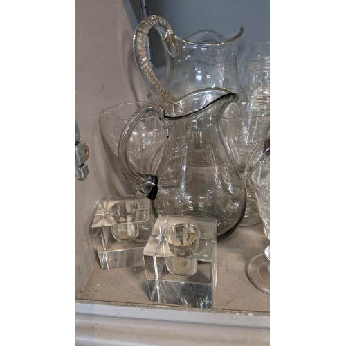 68 - A mixed lot of glassware to include a smoked glass jug, crystal cut decanters, a pair of cube style ... 