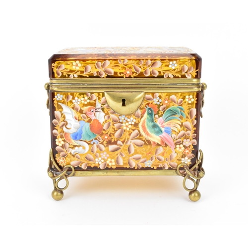 A brass-mounted Moser enamelled glass casket, late 19th/early 20th century, the rectangular amber glass body applied with polychrome enamel birds/mythical creature and profuse foliage, with pierced handles either side, raised on four brass intertwined feet
