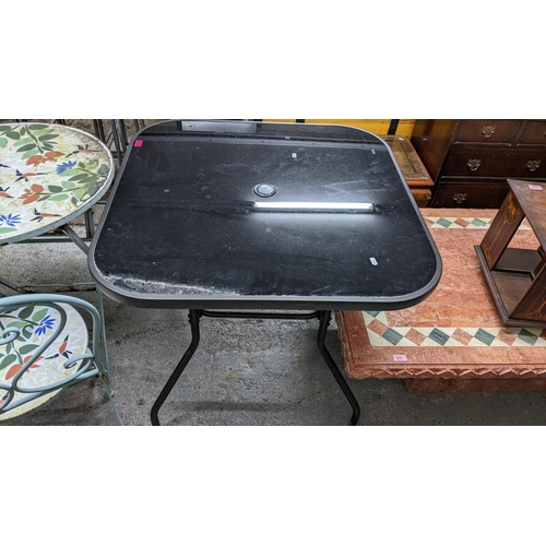 440 - A glass topped and grey coloured metal and plastic garden table, inset circular black coloured glass... 