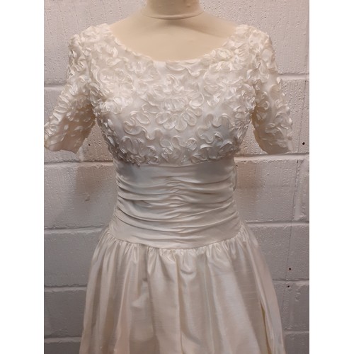 152 - A Donerica off white silk effect wedding dress having a zip fastening to the rear with large bow to ... 