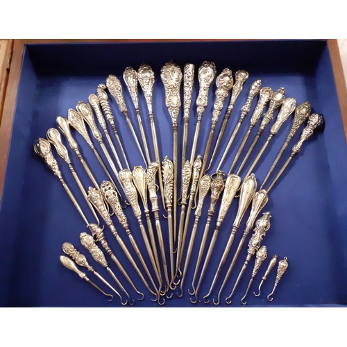 40 - A collection of silver and white metal button hooks housed in  a mixed hardwood table top display ca... 
