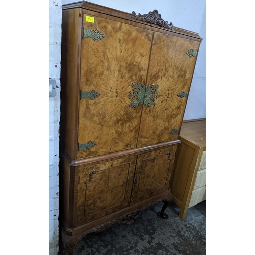 73 - A walnut drinks cabinet, carved pediment over twin doors with brass hinges and escutcheons, over fur... 