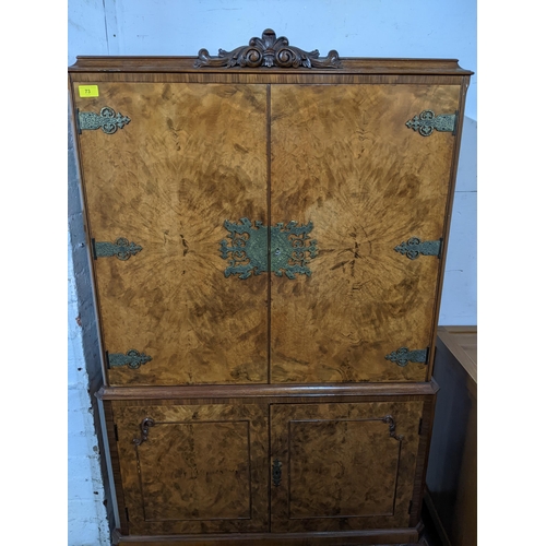 73 - A walnut drinks cabinet, carved pediment over twin doors with brass hinges and escutcheons, over fur... 