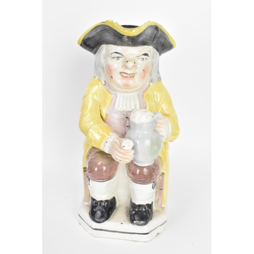 131 - An early 19th century Toby jug, typically modeled seated resting a foaming mug of ale on one knee an... 