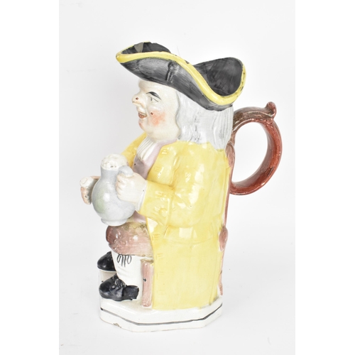 131 - An early 19th century Toby jug, typically modeled seated resting a foaming mug of ale on one knee an... 