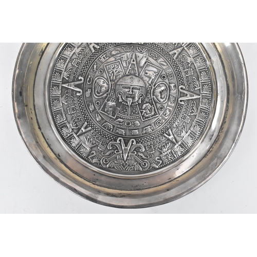 174 - A South American white metal dish having a raised edge and embossed decoration bearing the Aztec cal... 