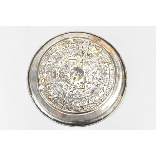 174 - A South American white metal dish having a raised edge and embossed decoration bearing the Aztec cal... 