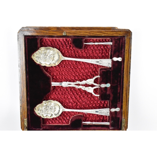 198 - A late Victorian oak cased silver plated dessert canteen, consisting of two berry spoons, grape scis... 