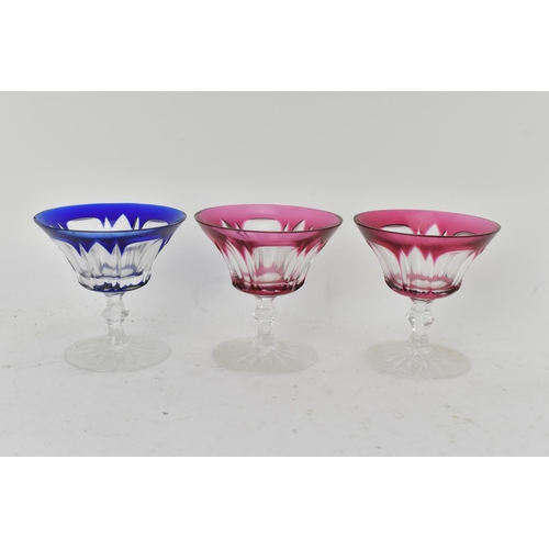 223 - A set of twelve Bohemian coloured coupe glasses having flashed bowls upon faceted and lobed stems an... 