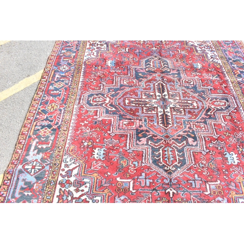 225 - A Persian Heriz hand woven rug, having a red ground with a central motif within a field of stylised ... 