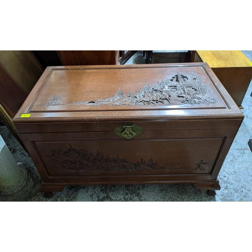 421 - An Asian camphor wood chest with carved landscape scene of figures on horseback and foot in front of... 