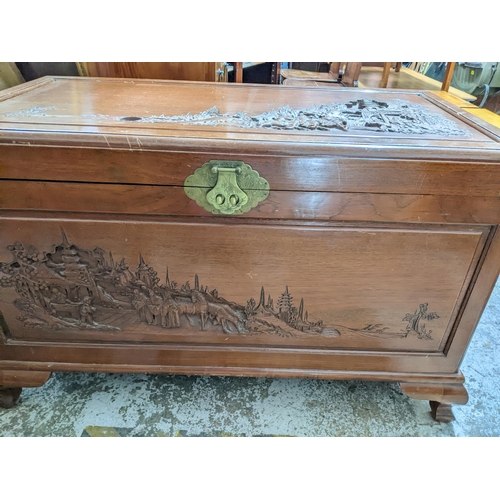 421 - An Asian camphor wood chest with carved landscape scene of figures on horseback and foot in front of... 