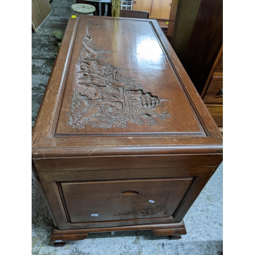 421 - An Asian camphor wood chest with carved landscape scene of figures on horseback and foot in front of... 