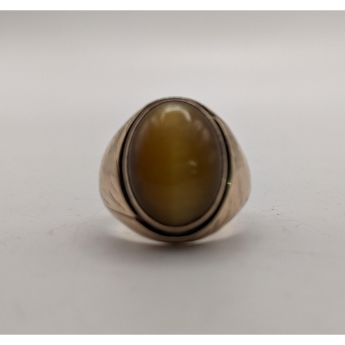 347 - A yellow metal gents ring set with a cabouchon tiger's eye, engraved design to the shoulders, unmark... 