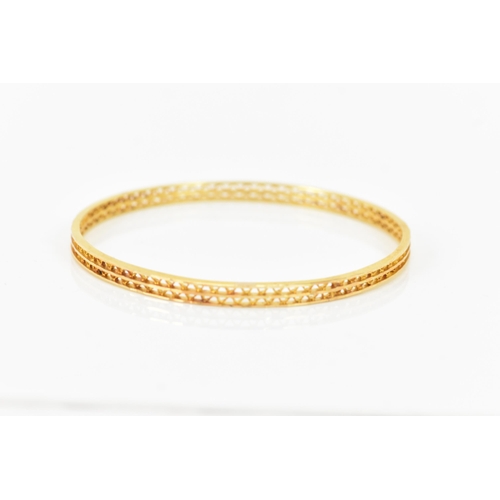 134 - An 18ct yellow gold bangle, having a pierced woven design and stamped N G F 18ct to the border, 7cm ... 