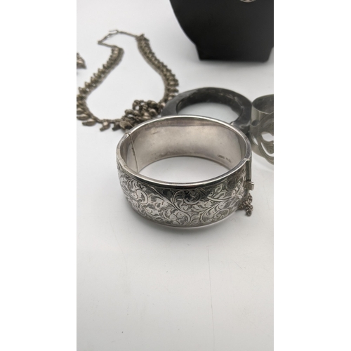 98 - A group of silver and white metal jewellery to include a silver hinged bangle with engraved floral d... 