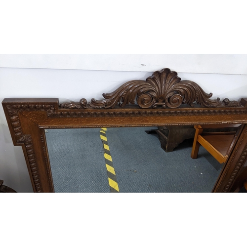 135 - An early 20th century oak wall hanging mirror with a scroll floral carved pediment, 72cm h x 91.5cm ... 